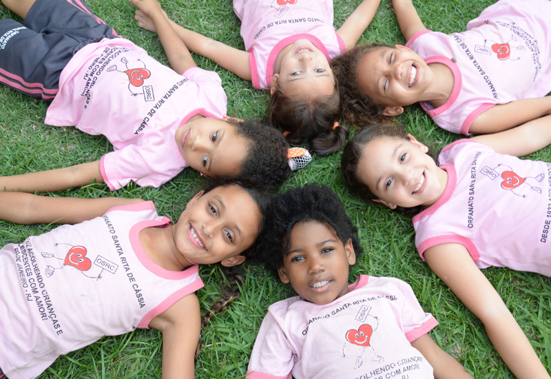 Seis meninas deitadas na grama com o uniforme do Orfanato Santa Rita de Cássia.